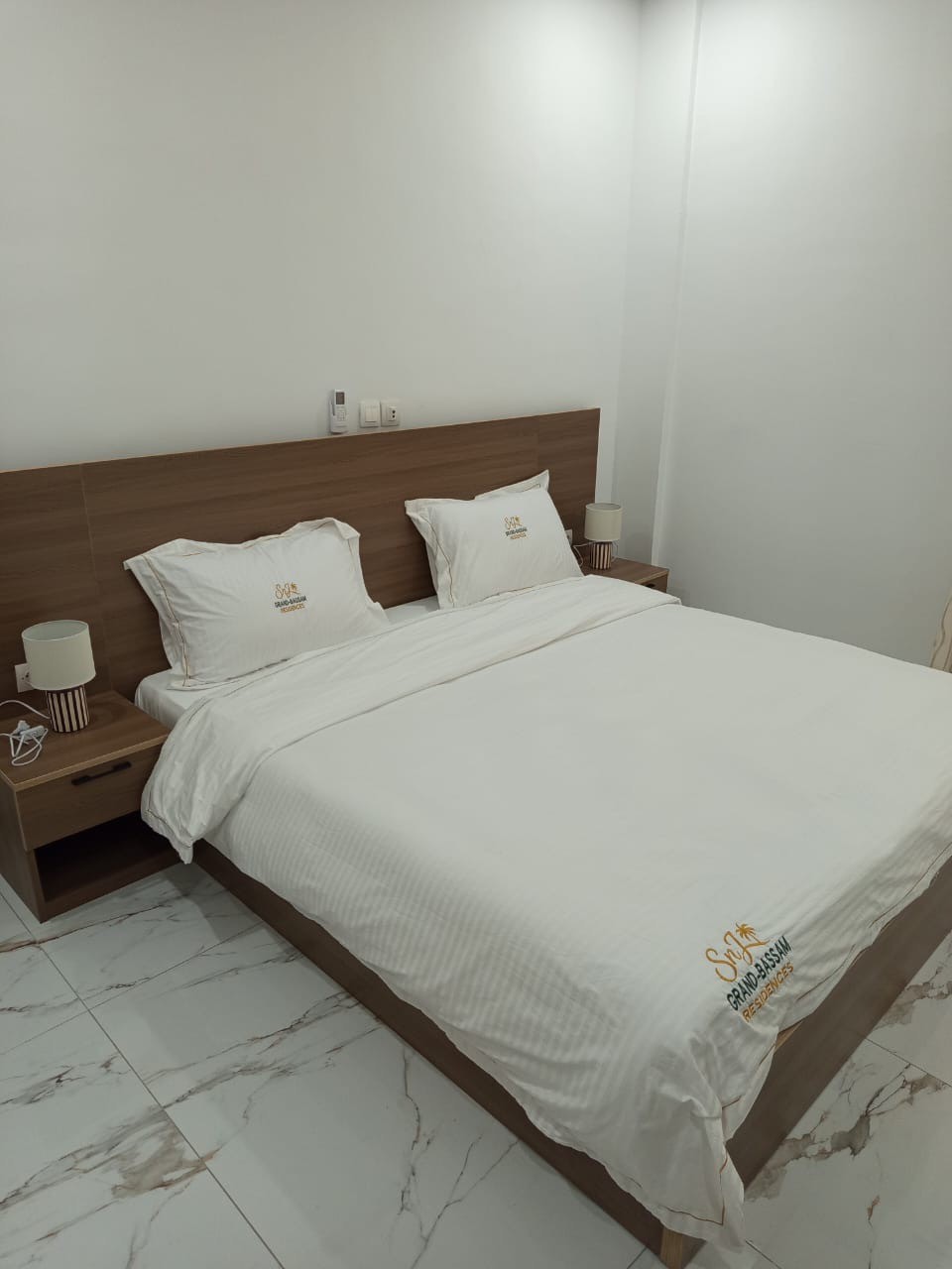 Chambre de SnJ Grand-Bassam Résidences avec lit double et linge brodé au nom de la résidence